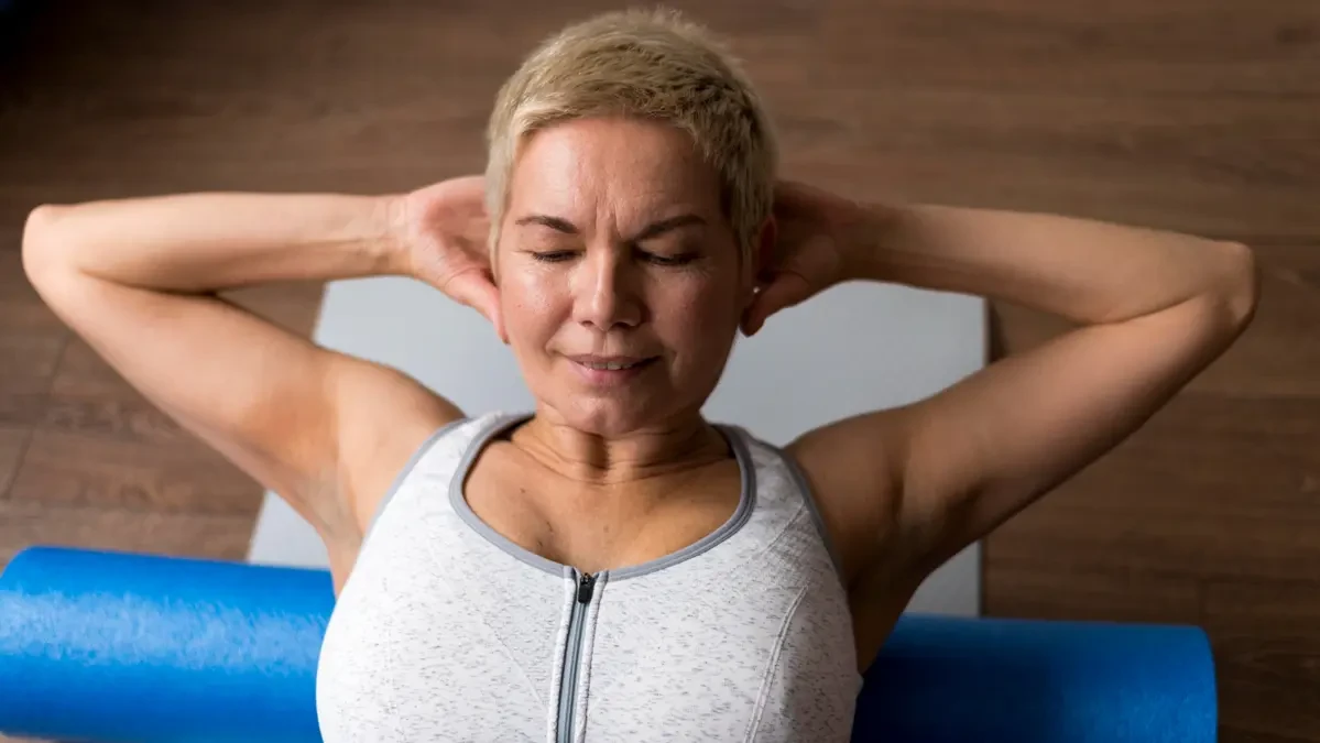 A middle-aged woman lying on a blue foam roller performing self-myofascial release on her upper back at home, representing the recommended evening foam rolling routine shown in a 2024 Scientific Reports study to support connective tissue recovery and reduce fascial stiffness before sleep.