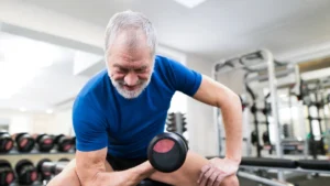 Older man lifting dumbbells in gym to prevent muscle loss after 50 through resistance training and proper protein intake.