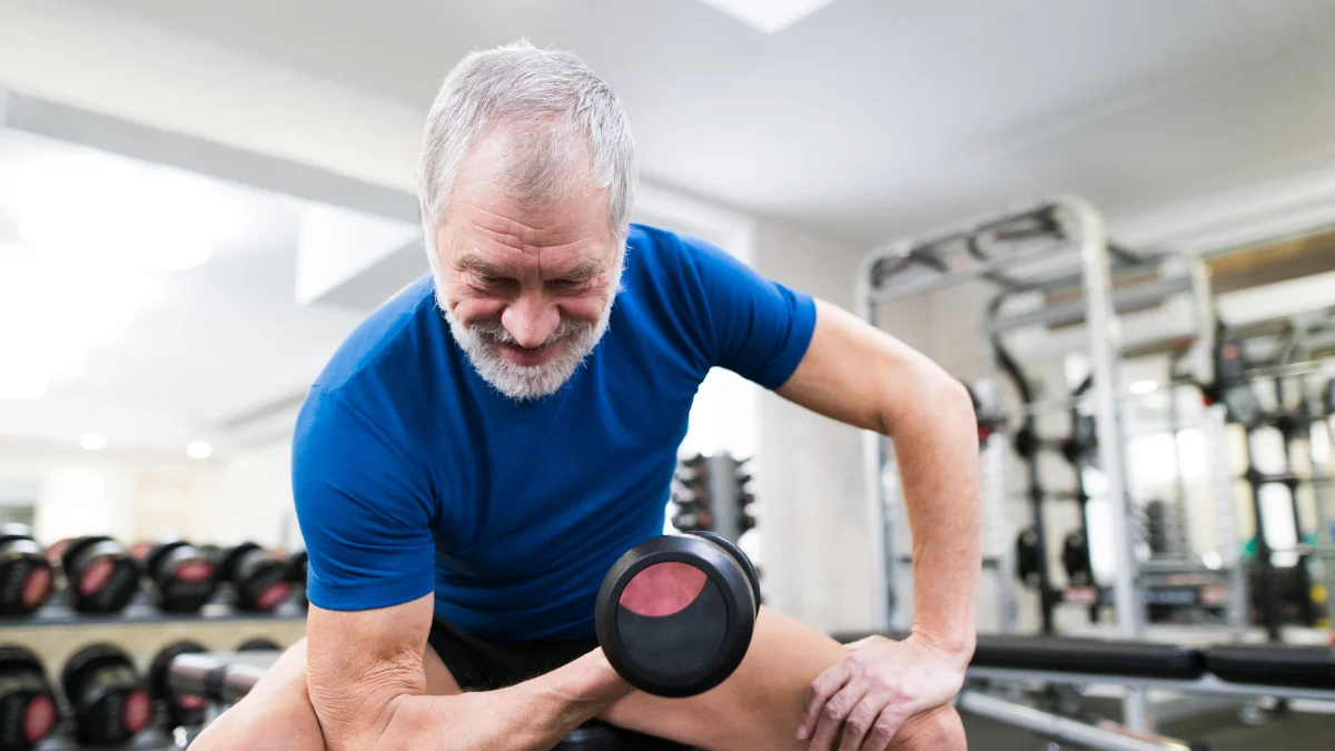 Older man lifting dumbbells in gym to prevent muscle loss after 50 through resistance training and proper protein intake.
