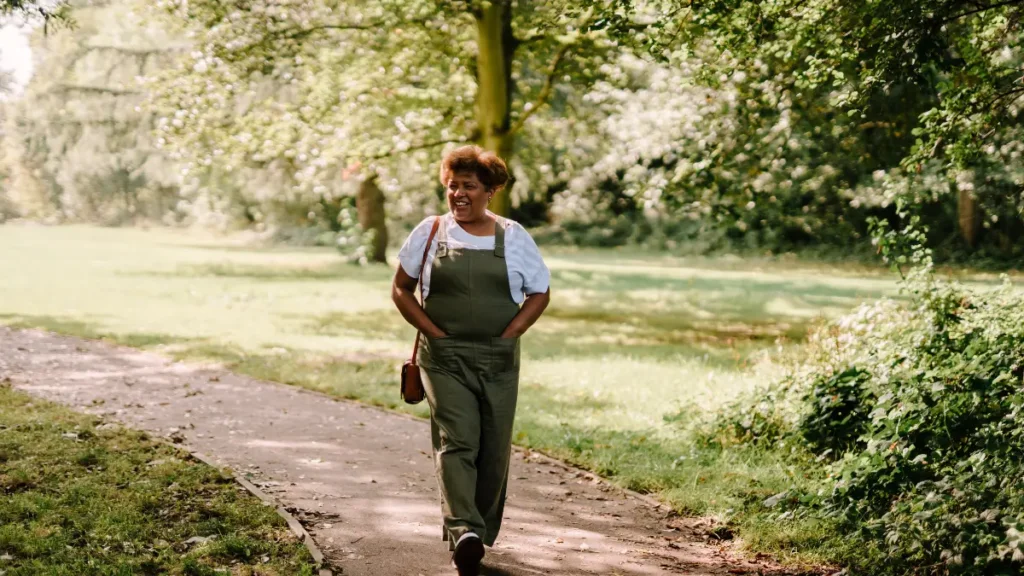 Woman in her early 60s walking along a tree-lined path, practicing daily movement linked to gut bacterial variety in older adults.