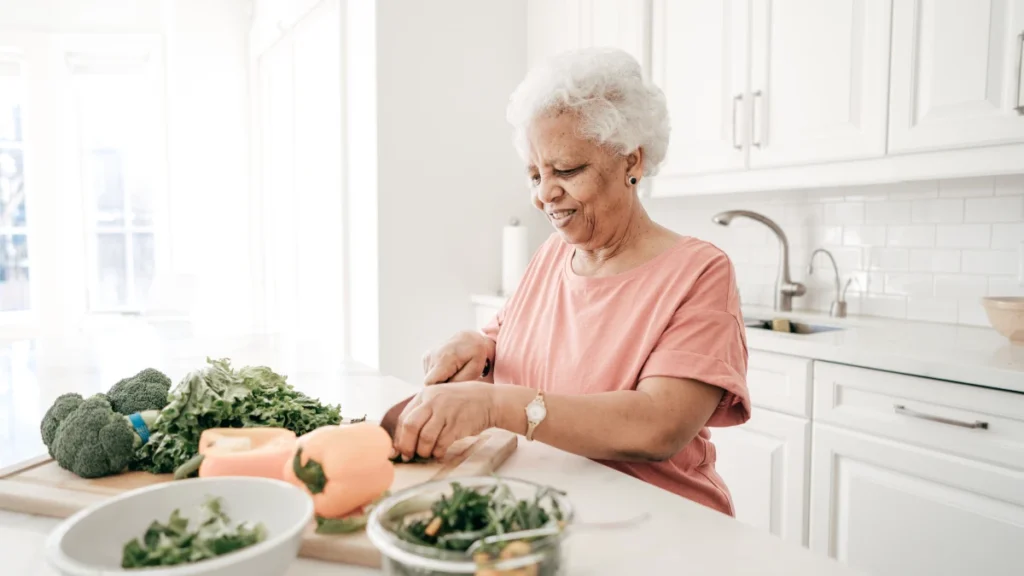 Black woman in her 70s chopping broccoli, bell pepper, and leafy greens at a bright kitchen counter, building a fiber-rich gut-healing meal plan after 50.