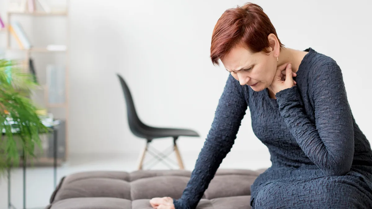 Mature woman sitting at home with a pained expression, signifying a potential angina symptom related to heart health