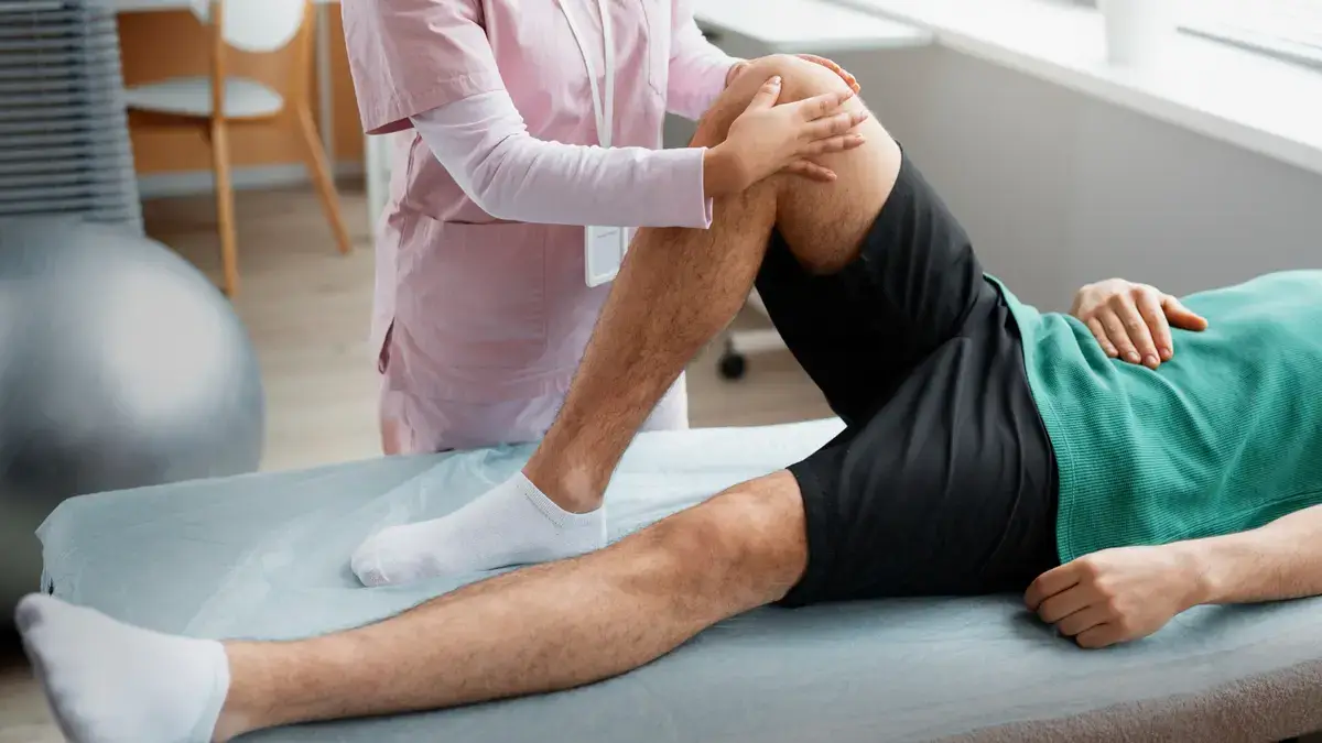 Physiotherapist examining a patient's bent knee during a clinical assessment on a treatment table in a medical setting.