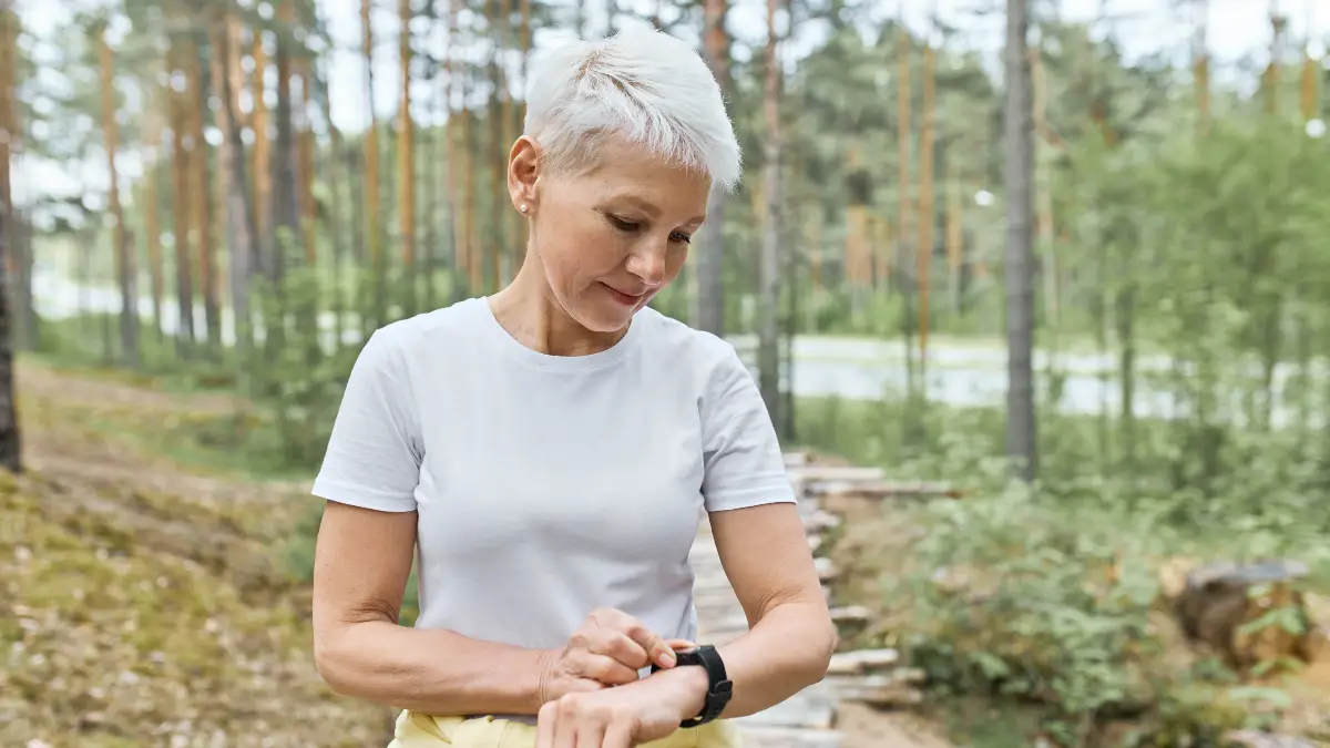 Mature woman tracking steps on a smartwatch during outdoor exercise, representing daily step count goals for adults over 60.