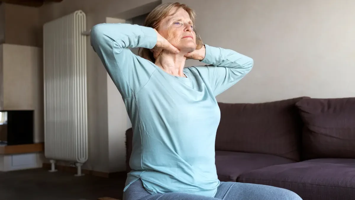 Mature woman performing a gentle overhead stretch in bed to relieve morning stiffness after 50.