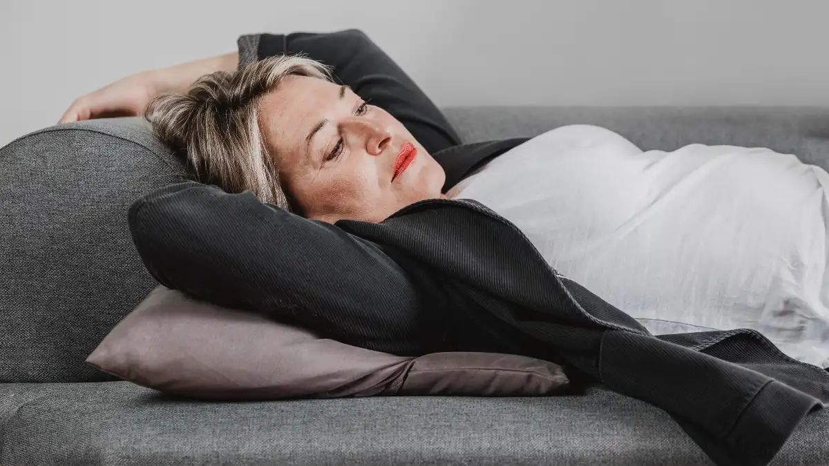 Mature woman lying on a sofa with a heavy expression of unexplained fatigue to illustrate low cellular energy output despite getting enough sleep.