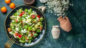 A chopped vegetable salad containing cheese and tomatoes rests on a dark blue surface to illustrate a calcium and oxalate dietary pairing for kidney health.