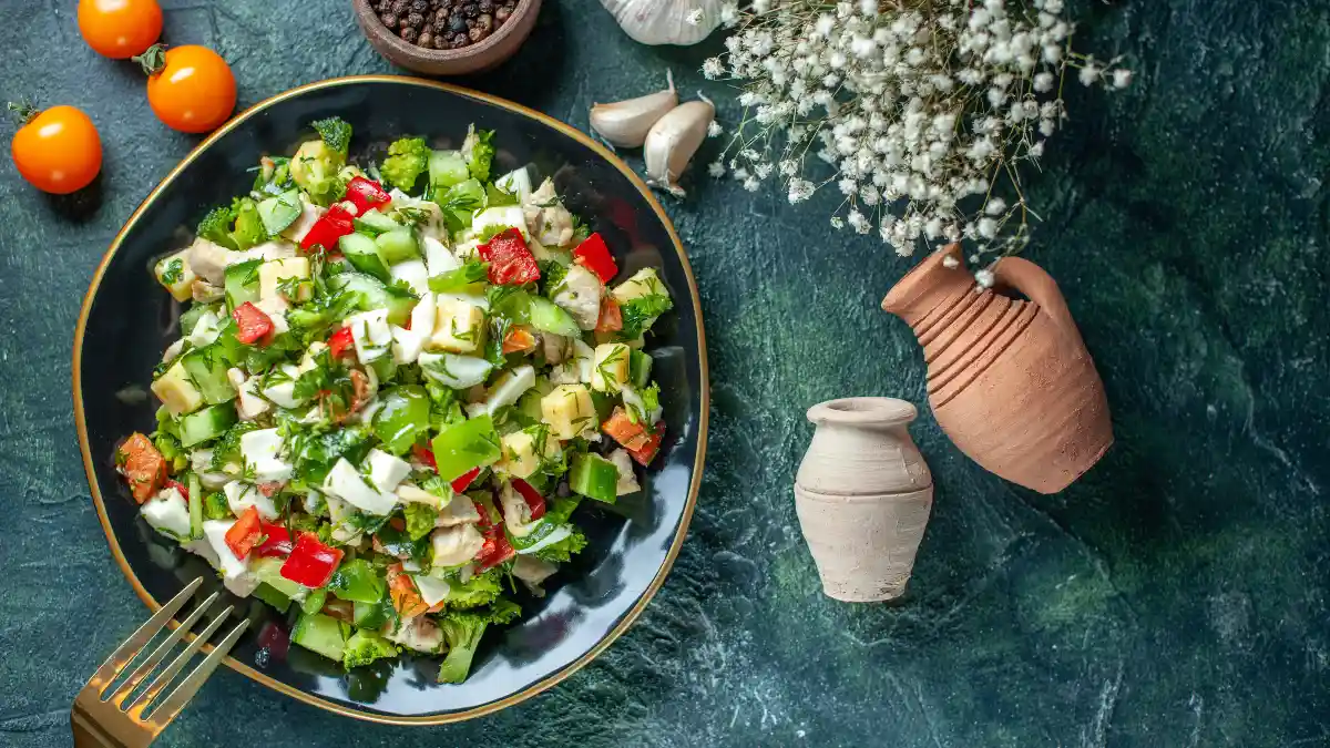A chopped vegetable salad containing cheese and tomatoes rests on a dark blue surface to illustrate a calcium and oxalate dietary pairing for kidney health.