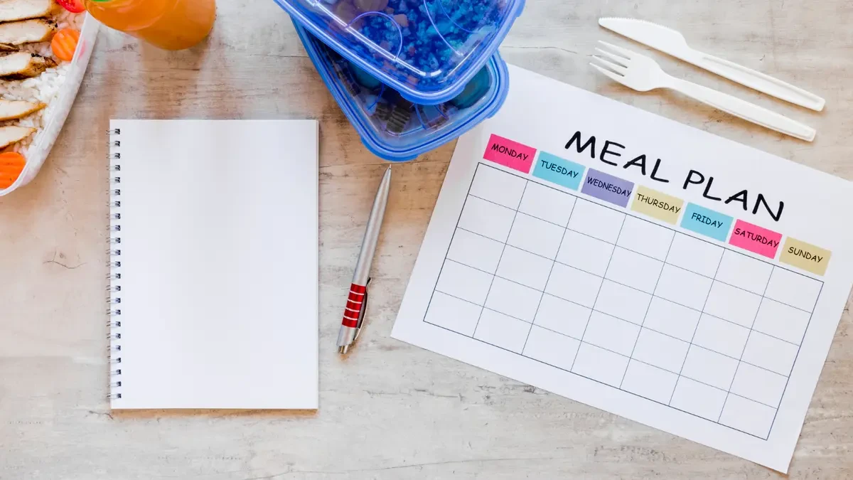 Weekly meal plan sheet and notebook on a desk, representing a simple starting protocol for boosting nitric oxide levels