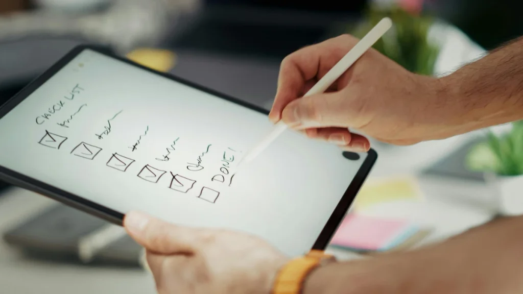 Person writing a weekly training checklist on a tablet to track a fall prevention exercise schedule.
