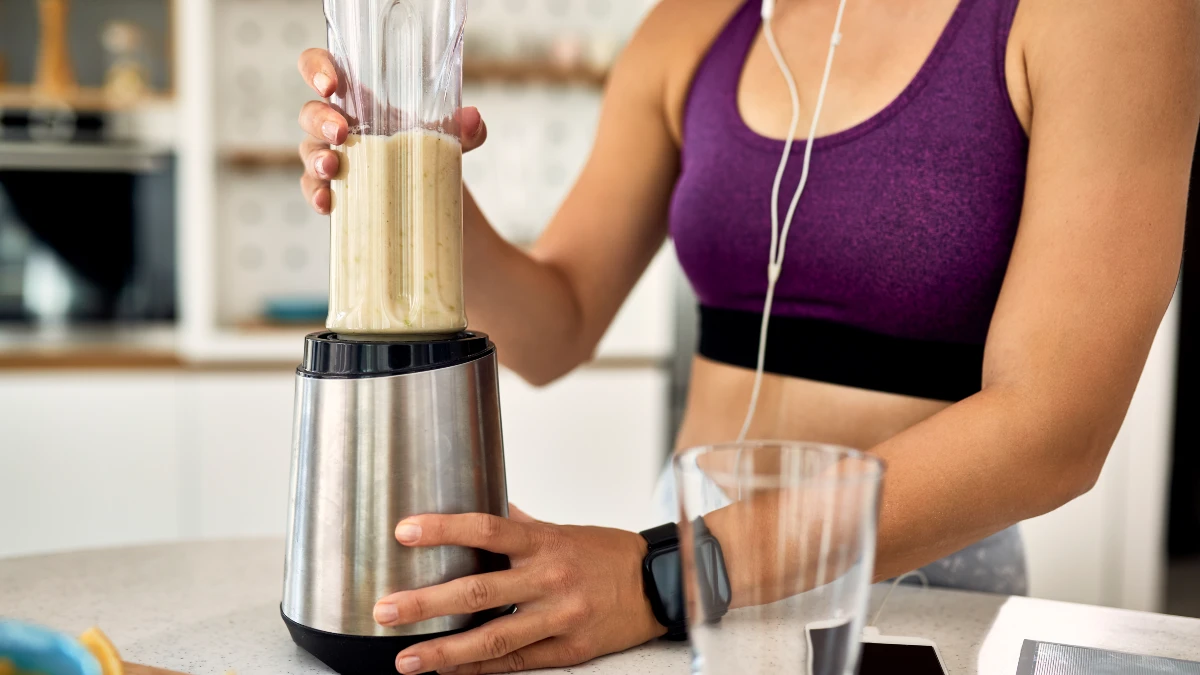 Mature woman in kitchen prepares high-protein smoothie to support basal metabolic rate by fueling muscle-building cellular energy.
