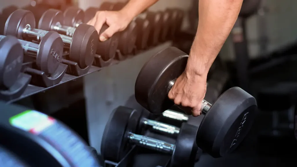 Hands lifting heavy dumbbells off a gym rack to illustrate progressive overload and smart training weight selection after 50.