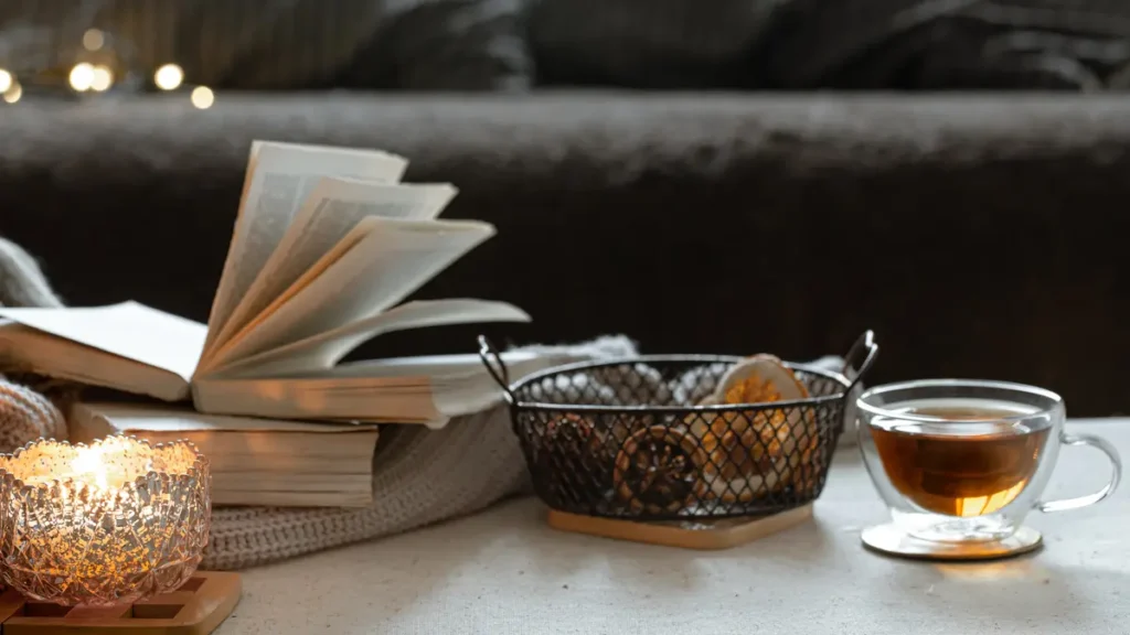 Printed book, herbal tea, and candle on table at night — simple bedtime swaps that support deep sleep after 50.
