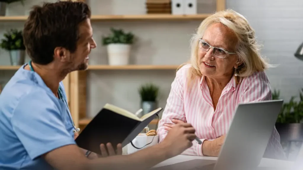 Mature woman sitting attentively across from a partially visible healthcare professional, leaning forward with a focused expression as she discusses treatable causes of memory changes after 60.