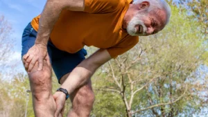 Mature fitness enthusiast gripping his leg during outdoor movement to manage unexpected delayed muscle soreness.
