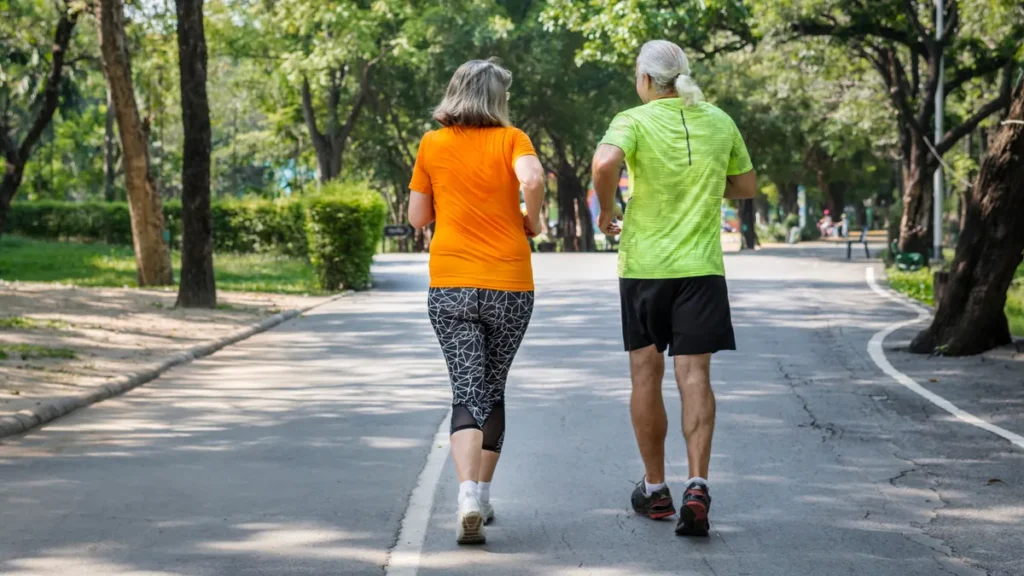 Older couple walking briskly along a sunlit park path from a rear view to blunt an afternoon blood glucose spike.