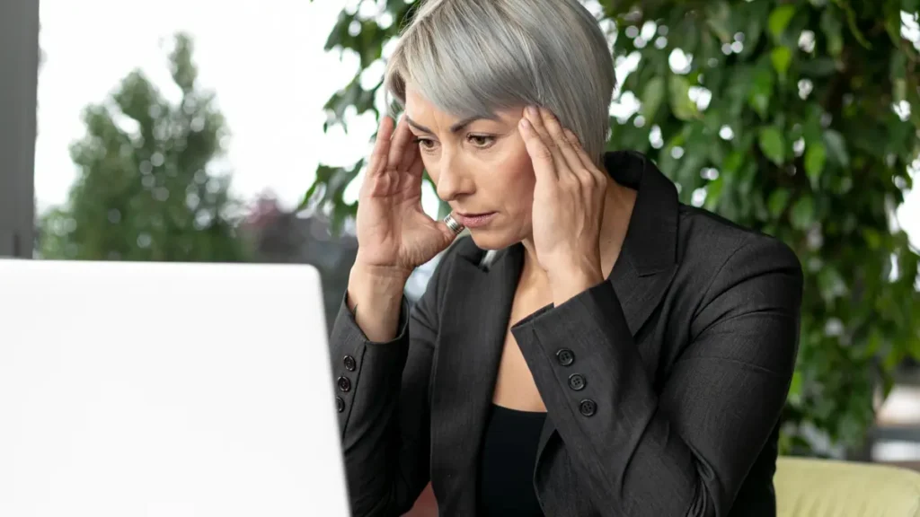 Mature woman experiencing high stress and distraction at her desk, illustrating how pushing through mid-morning hunger spikes cortisol management issues.