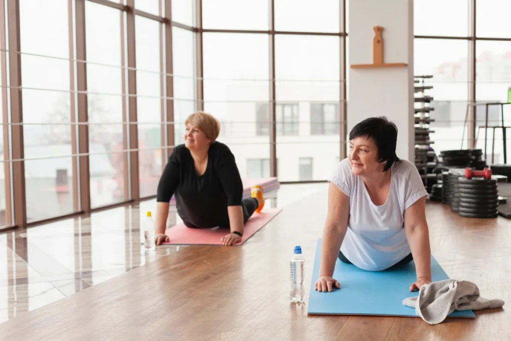 Two mature women participating in a structured exercise class together to build a healthy routine and support a sense of purpose.