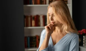 Mature woman with blonde hair looking deeply concerned and pensive, reflecting on unexplained strength loss and the effects of anabolic resistance.