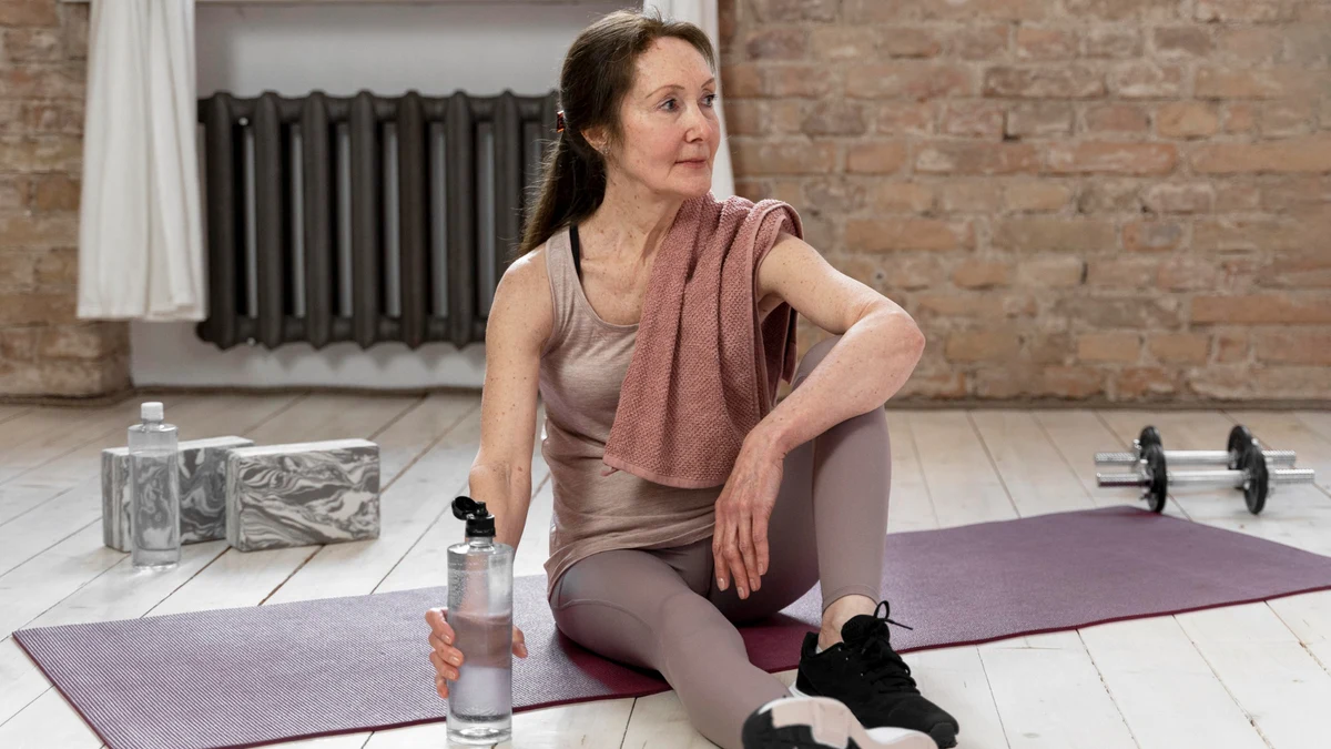 Woman in her late 50s resting between sets on a workout mat, reflecting the experience of why the body stops responding to exercise after 50.