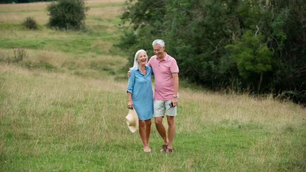 A smiling senior couple walking through a green meadow, showing light daily movement as an anti-inflammatory strategy for healthy aging.