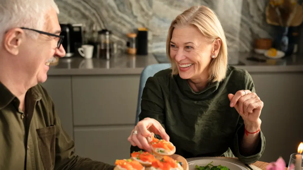 Mature couple laughing while sharing a high-quality protein meal of salmon to support 24 hour muscle protein synthesis rates.