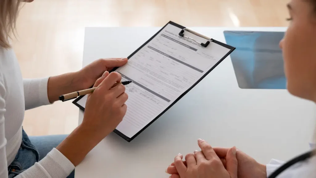 Woman filling out a medical questionnaire on a clipboard during a doctor's appointment, illustrating how perimenopause symptoms are screened for depression.