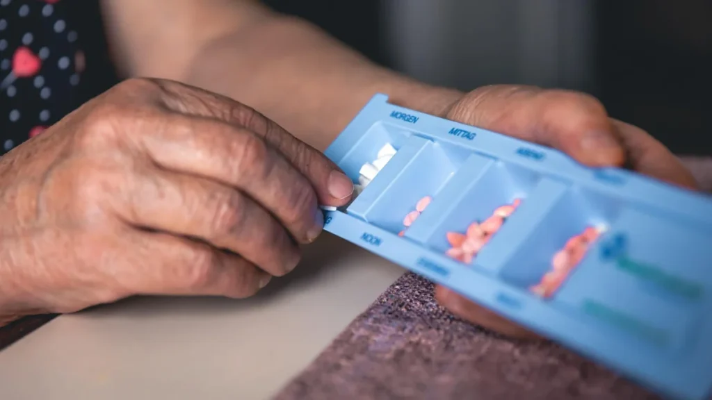 Hands organizing daily supplements into a pill case to manage dosage timing.
