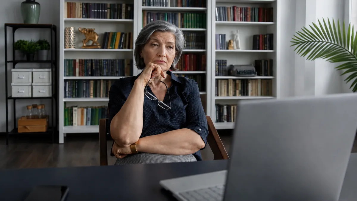 Woman in her late 50s sitting at a home desk in afternoon light with an unfocused expression, reflecting the blood sugar and willpower after 50 afternoon energy crash.