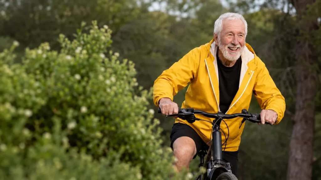 A senior man cycling outdoors in a yellow jacket, representing moderate aerobic exercise that supports memory and brain health after 50.
