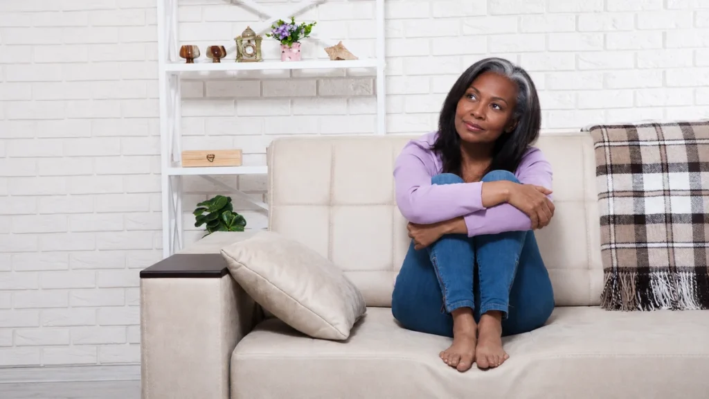 Mature woman with silver hair pausing on a sofa while navigating unstructured free time after retiring.
