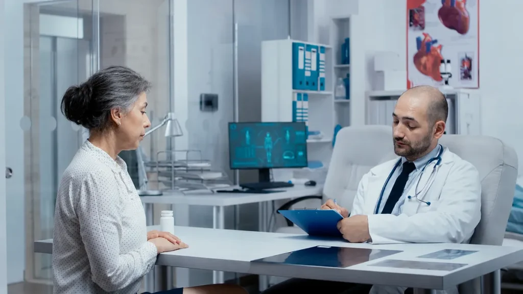 Mature patient speaking with a cardiologist holding a blue clipboard to discuss unmeasured heart health risks.