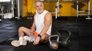 A mature man pauses on the gym floor during a hard workout to address training plateaus caused by anabolic resistance after 50.