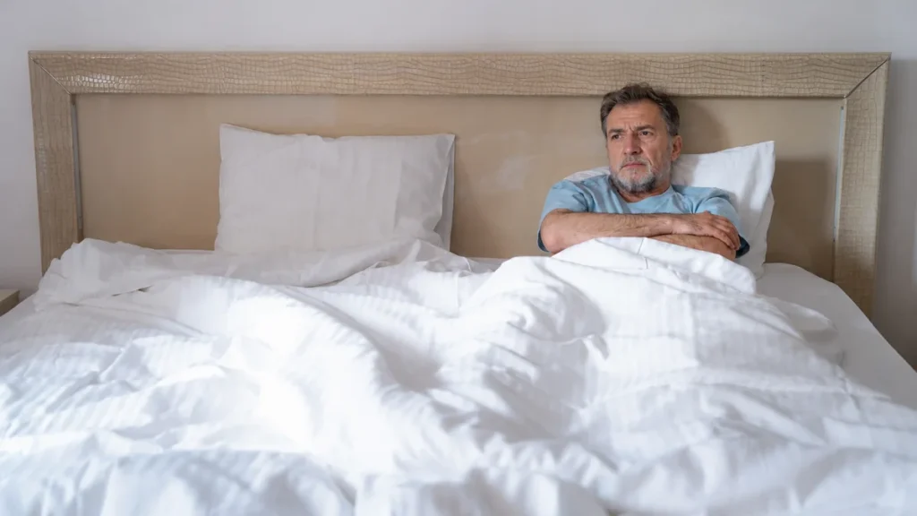 Mature man lying awake in bed with arms crossed, experiencing circadian rhythm phase advance that triggers early morning wakefulness.