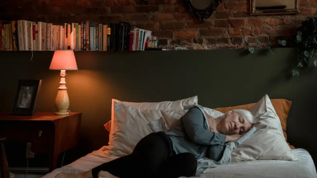 An older woman sleeping on her side in a warmly lit bedroom, representing the role of deep sleep in muscle repair and recovery after 50.