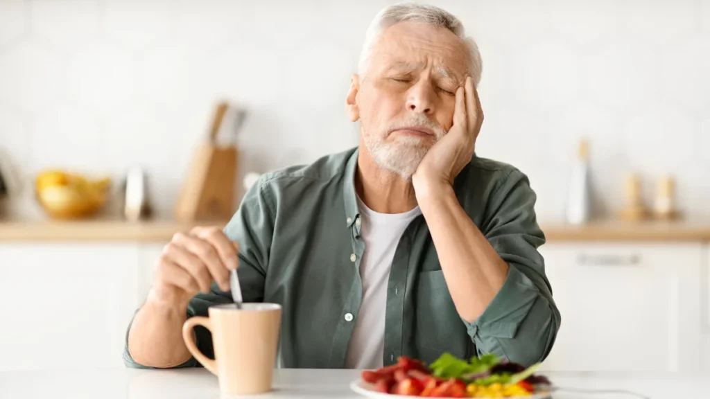 Older man looking fatigued at breakfast table with coffee, showing how aging affects blood sugar and morning focus after 50.