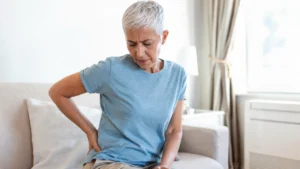 Woman pressing her hand into her right hip on a sofa, experiencing piriformis syndrome discomfort at home.