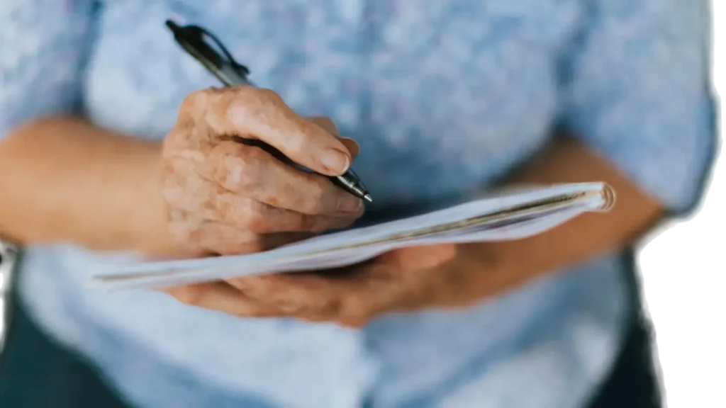 Hands of an older adult writing dates in a small journal to actively track cognitive patterns, creating a tangible memory log to share during their next doctor's visit.