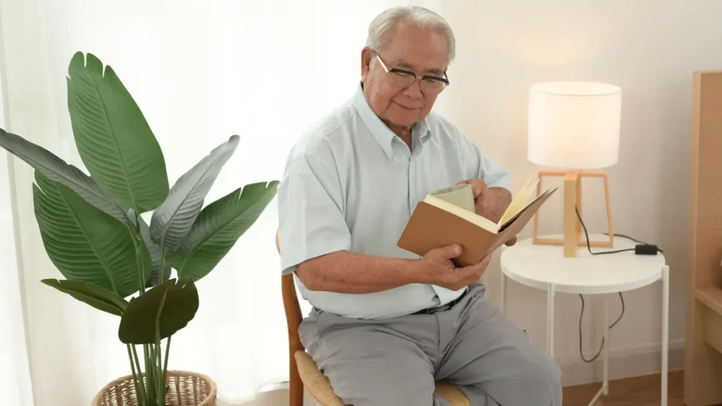 Mature man focused on a book and holding a coffee mug in a sunlit room, illustrating a quiet cognitive task that benefits from optimized post-exercise timing