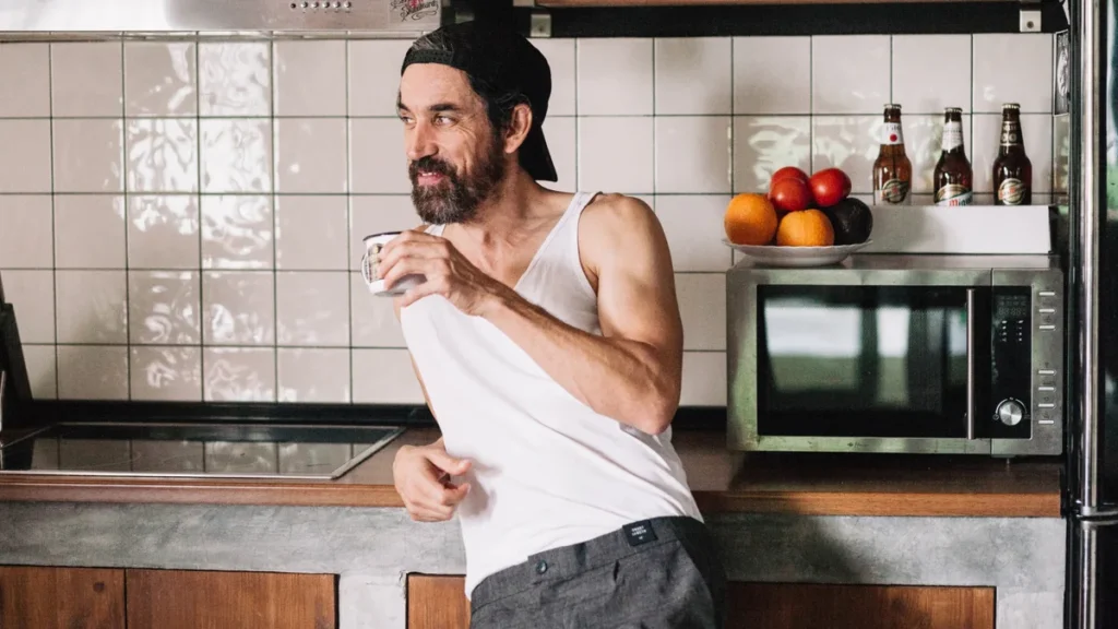 Mature man smiling while holding a white mug in a bright kitchen to maintain realistic daily wellness routines.