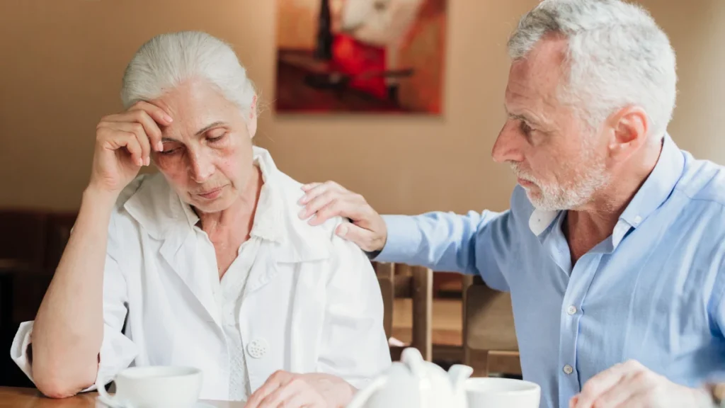 Older couple sitting together as a woman appears worried about memory changes while her partner offers support.