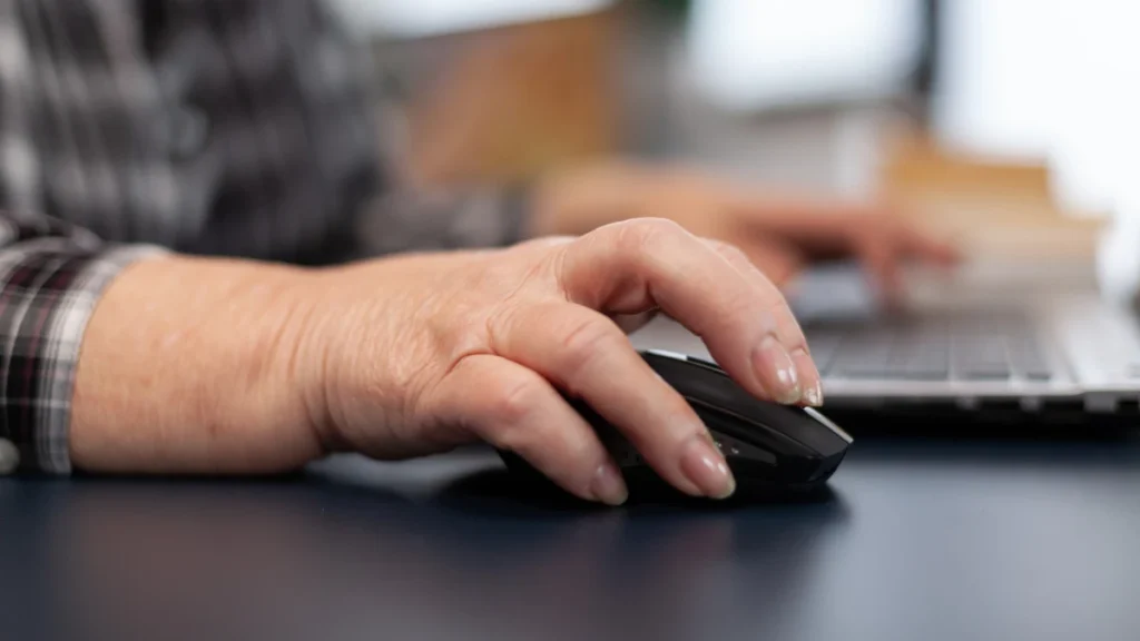 Close-up of a mature hand on a computer mouse preparing for an online reaction time test.