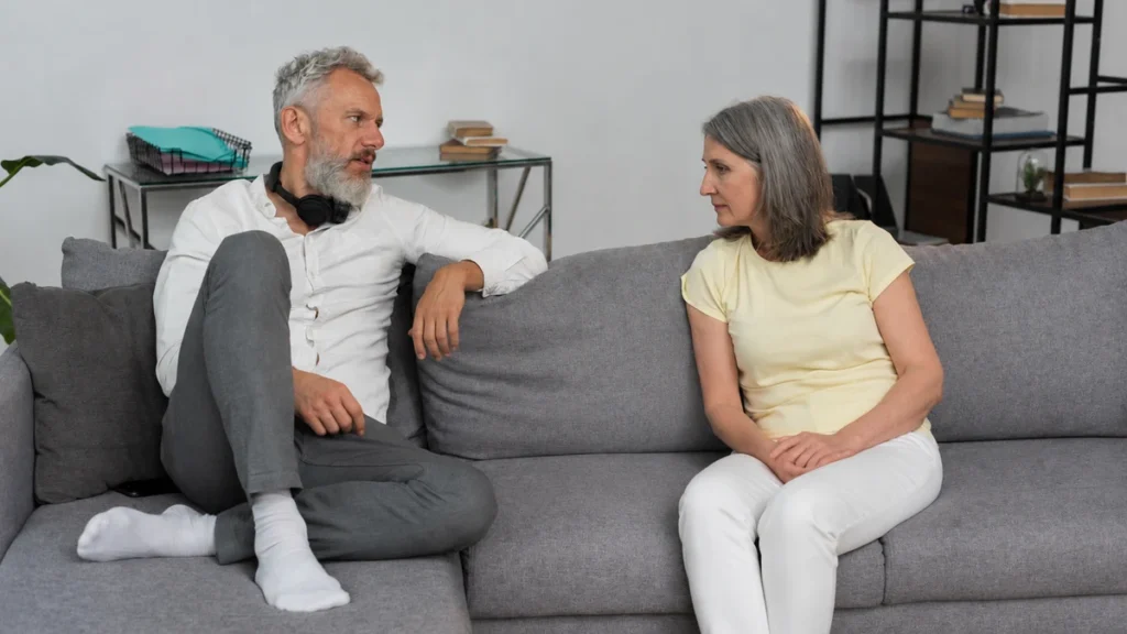Mature couple engages in an earnest conversation on a sofa about recent changes in sleep habits.