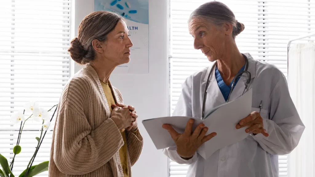 Mature woman in a knit cardigan reviews clinical data alongside her physician during an earnest consultation.