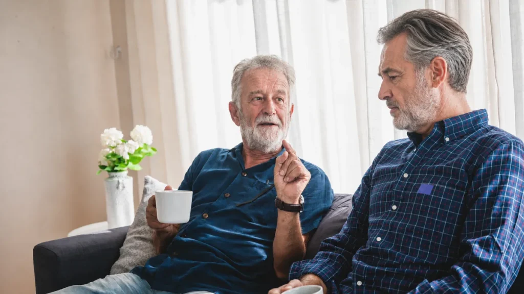 Two mature men talking over coffee on a couch, showing an authentic moment of connection between generational peers.