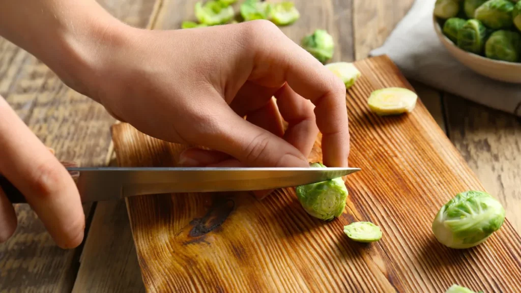 Close-up of hands slicing fresh Brussels sprouts on a wooden cutting board to prepare goitrogenic vegetables after 50.