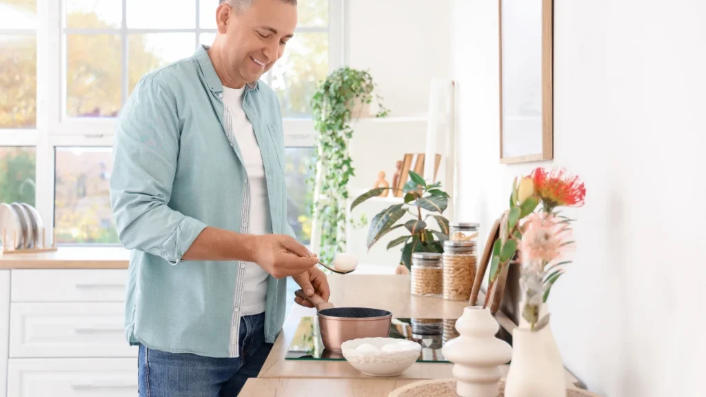 Content mature man lifting a boiled egg from a pot in a bright kitchen to front-load his breakfast protein.