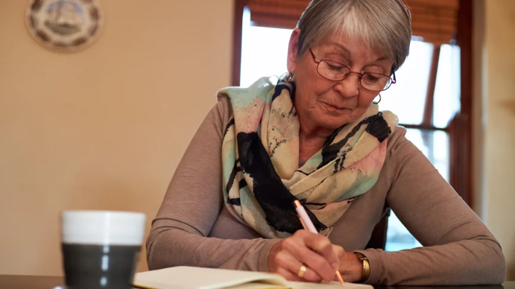 Mature woman in glasses writing in her notebook to plan her gradual step-down heart-burn medication taper.