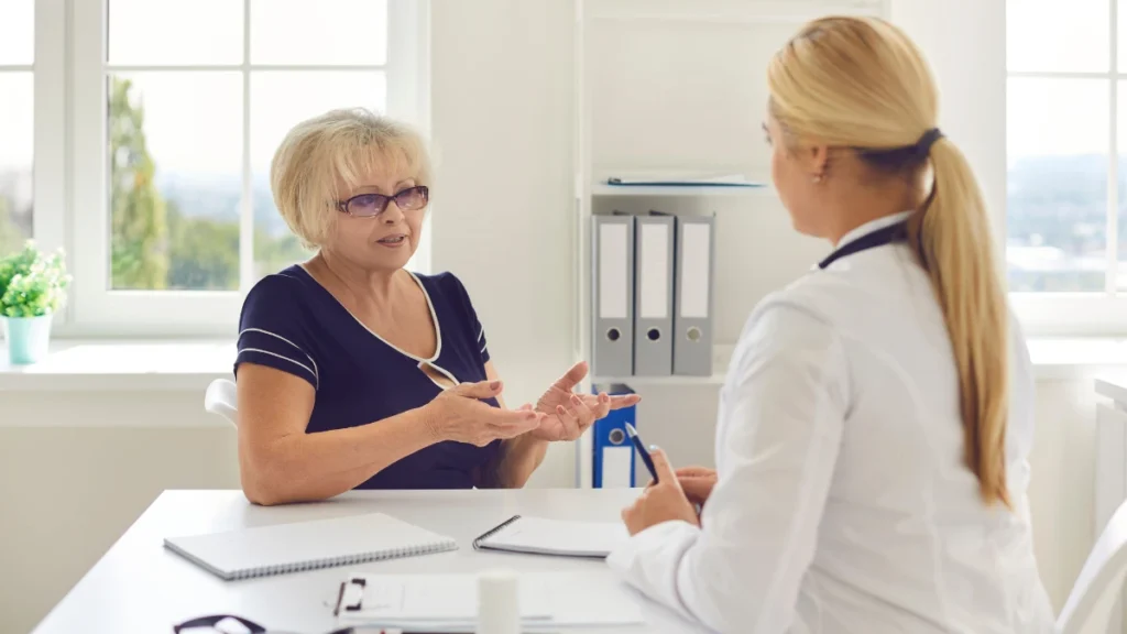 Mature patient discussing her lab results with a female doctor in a bright office to identify underlying metabolic blocks.