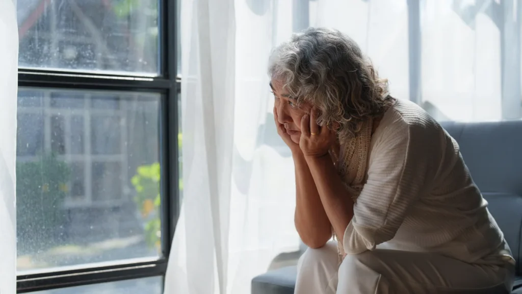 Weary mature woman resting her head in her hands by a window, seeking answers for fatigue in women over 55.